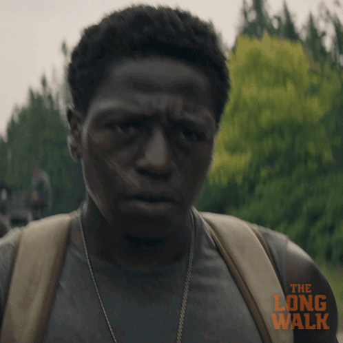 A Man Is Wearing A Backpack And A Shirt That Says The Long Walk On It GIF