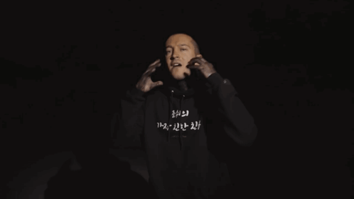 A Man Is Wearing A Black Hoodie With Korean Writing On The Front GIF