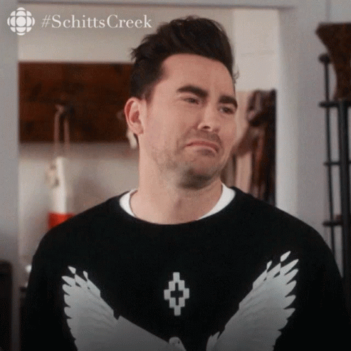 A Man Is Wearing A Black Sweater With White Wings On The Front GIF