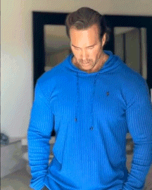 a man is wearing a blue hoodie and standing in front of a mirror .