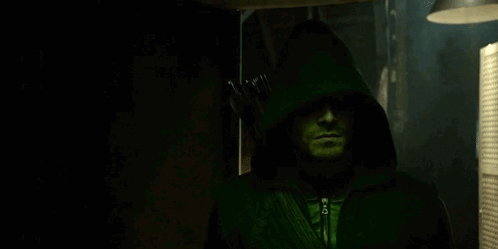 A Man Is Wearing A Green Hooded Jacket And Holding An Arrow . GIF