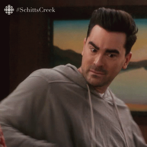 A Man Is Wearing A Grey Hoodie And The Word Schitts Creek Is On The Bottom Right GIF