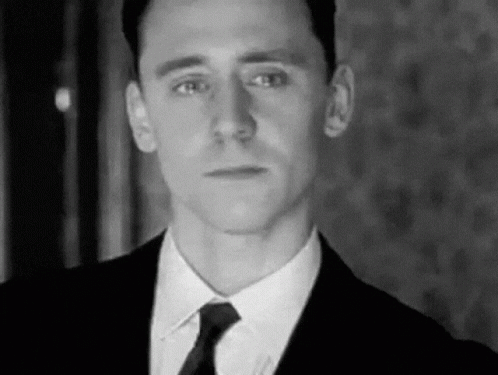 A Man Is Wearing A Suit And Tie And Looking At The Camera . GIF