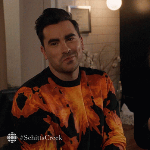 A Man Is Wearing A Sweater That Says Schitts Creek On The Bottom GIF