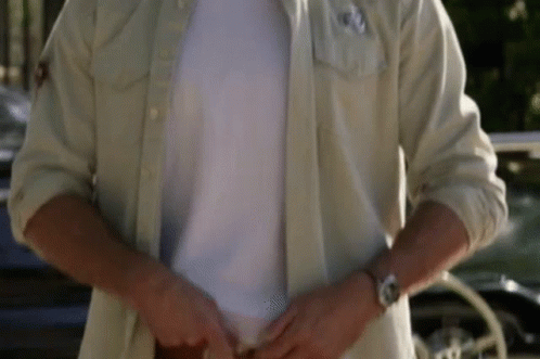 a man is wearing a white shirt and a watch while standing in front of a car .