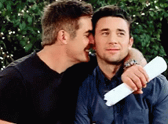 A Man Is Whispering Into Another Man 'S Ear While Holding A Piece Of Paper GIF