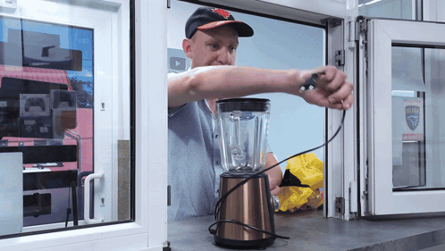 A Man Is Working On A Blender In Front Of A Window That Has A Sticker That Says ' Safety ' GIF