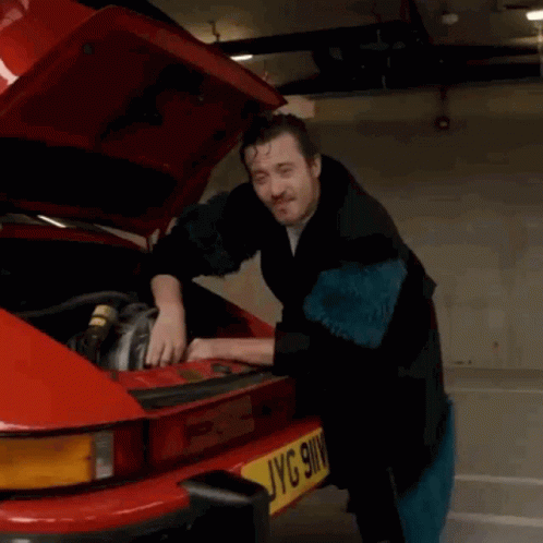 A Man Is Working On A Red Car With The Hood Up And A License Plate That Says Jyg 9Wv GIF