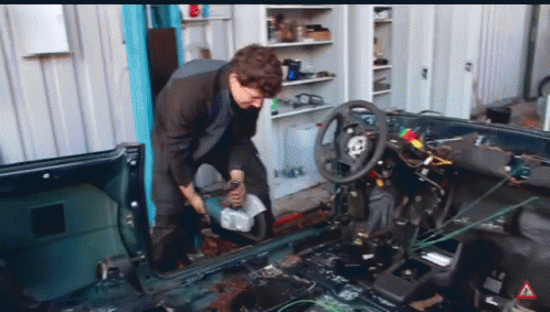 A Man Is Working On The Inside Of A Car With A Warning Sign In The Corner GIF