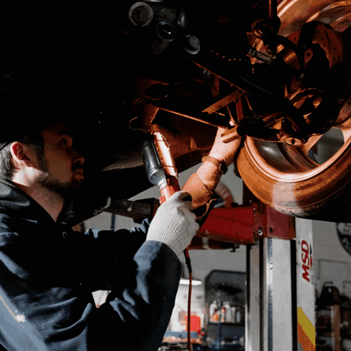 A Man Is Working Under A Car In A Garage With A Msd Lift In The Background GIF