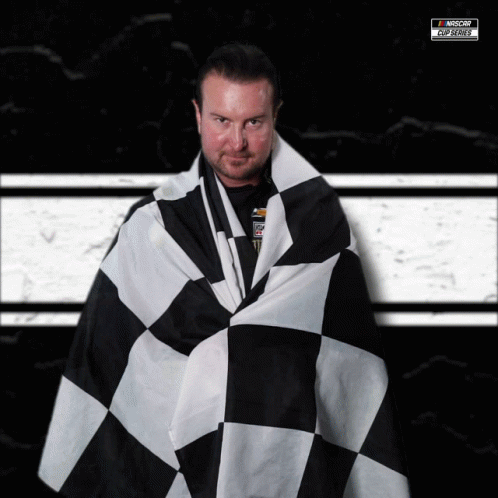 A Man Is Wrapped In A Black And White Checkered Flag With A Nascar Logo In The Background GIF