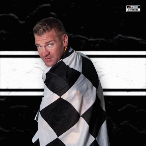 A Man Is Wrapped In A Black And White Checkered Flag With A Nascar Logo On The Bottom Right GIF