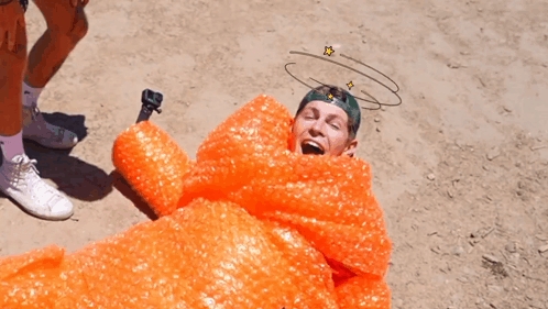 A Man Is Wrapped In Orange Bubble Wrap With A Drawing Of Stars On His Head GIF