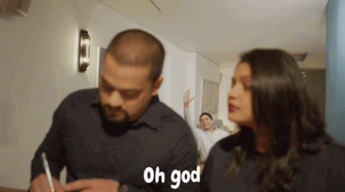 A Man Is Writing On A Piece Of Paper While A Woman Looks On And Says " Oh God " GIF