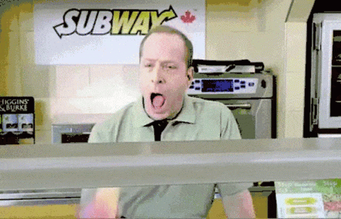 A Man Is Yawning In Front Of A Sign That Says Subway GIF
