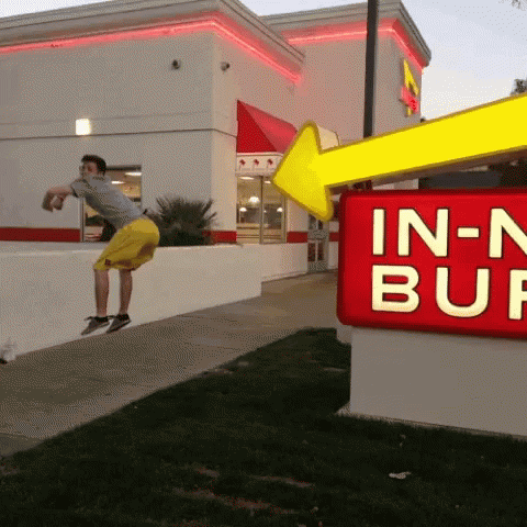 A Man Jumps In The Air In Front Of An In-N-Out Burger Sign GIF