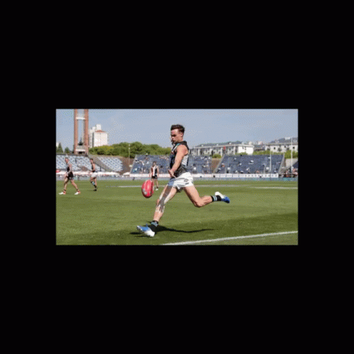 A Man Kicking A Soccer Ball On A Field With A Stadium In The Background GIF