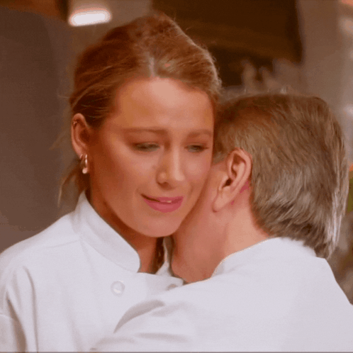 A Man Kisses A Woman On The Cheek While Wearing A Chef 'S Coat GIF