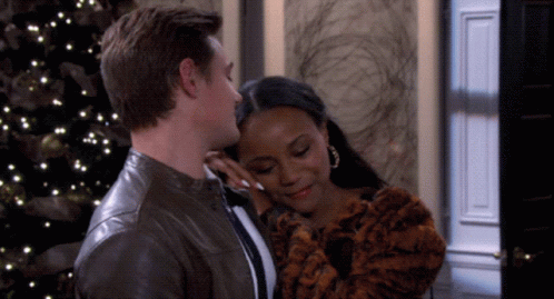 A Man Kisses A Woman On The Forehead In Front Of A Christmas Tree GIF