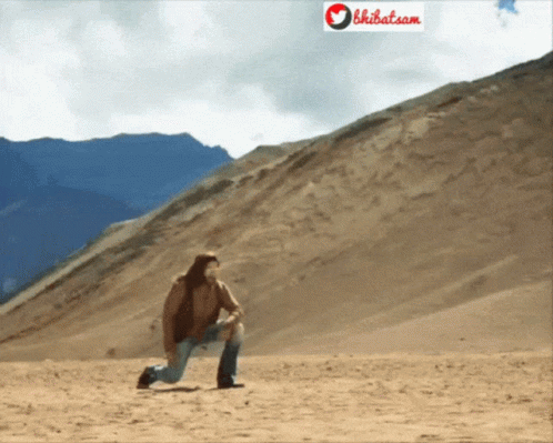 A Man Kneeling Down In The Desert With A Sign That Says Bhibat.com Behind Him GIF