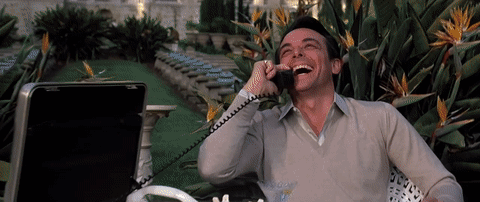 A Man Laughs While Talking On A Phone Outside GIF