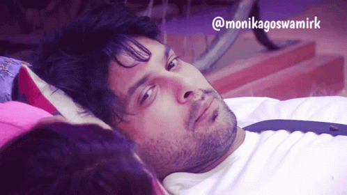 A Man Laying On A Bed Next To A Woman With The Name Monikagoswamirk On The Bottom Right GIF