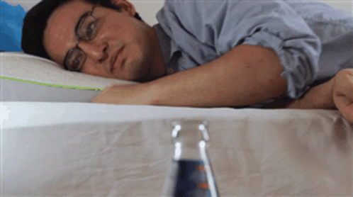 A Man Laying On A Bed With A Bottle Of Water In The Foreground GIF