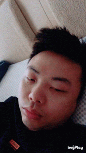 A Man Laying On A Bed With His Eyes Closed And A Label On His Shirt That Says ' I Am A ' GIF
