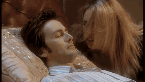 A Man Laying On A Bed With His Eyes Closed While A Woman Looks On GIF