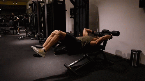 A Man Laying On A Bench In A Gym With A Machine That Says Technogym GIF