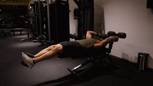 A Man Laying On A Bench In A Gym With A Machine That Says Technogym On It GIF