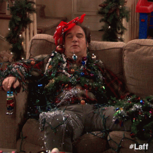 A Man Laying On A Couch Covered In Christmas Lights And Tinsel GIF