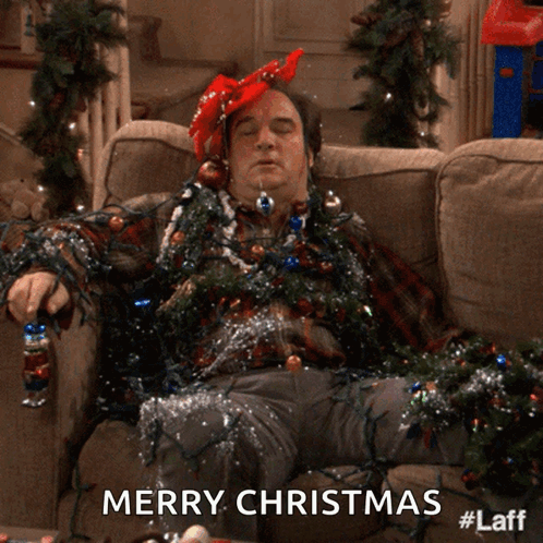 A Man Laying On A Couch Covered In Christmas Lights With The Words Merry Christmas Below Him GIF