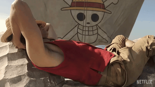 A Man Laying On A Rock In Front Of A Netflix Flag GIF