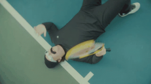 A Man Laying On The Ground Holding A Wilson Tennis Racquet GIF