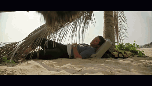 a man laying under a palm tree on the beach