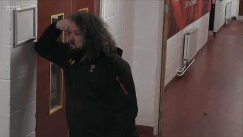 A Man Leaning Against A Wall In A Hallway With Bbc Written On The Corner GIF