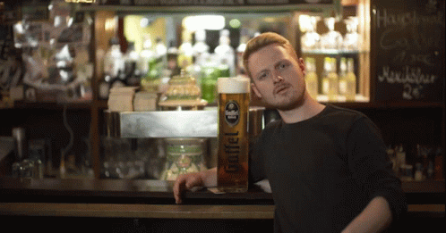 a man leans against a bar with a glass of goffel beer in front of him