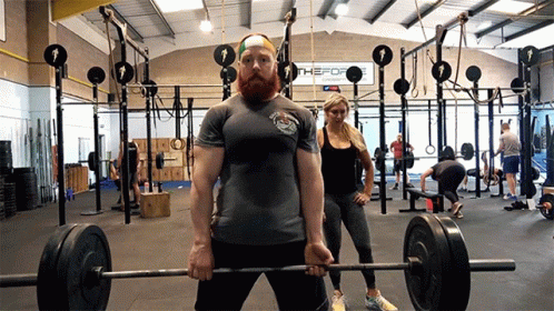 A Man Lifting A Barbell In A Gym With A Sign That Says The Fort GIF