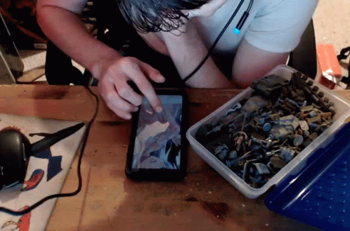 A Man Looking At A Picture On A Cell Phone Next To A Box Of Toy Soldiers GIF