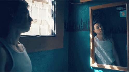 A Man Looking At His Reflection In A Mirror With A Sign On The Wall That Says ' A ' On It GIF