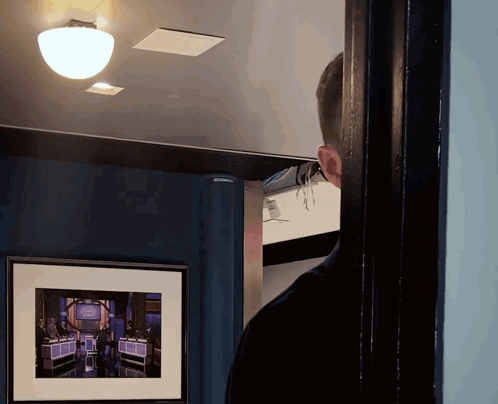 A Man Looking Through A Doorway At A Framed Picture Of A Game Show Called The Price Is Right GIF