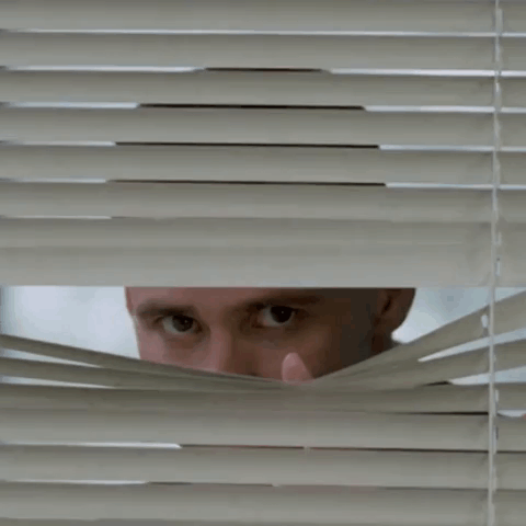 A Man Looking Through Blinds With His Hand On His Face GIF