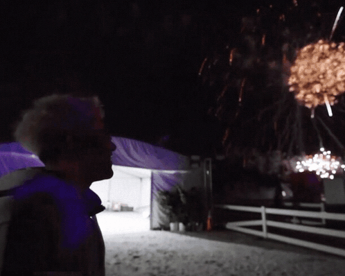 A Man Looks Up At A Fireworks Display In The Night Sky GIF