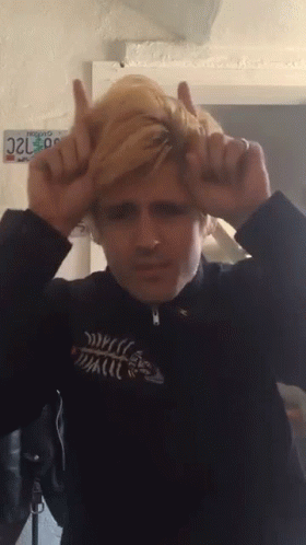 A Man Making A Devil Horns Gesture With A California License Plate Behind Him GIF