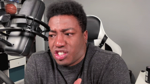 A Man Making A Funny Face In Front Of A Microphone With A Basketball On The Wall Behind Him GIF