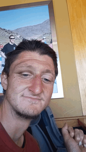 A Man Making A Funny Face In Front Of A Picture Of Two Men GIF