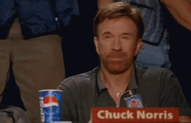 A Man Named Chuck Norris Is Sitting At A Table With His Fist In The Air GIF