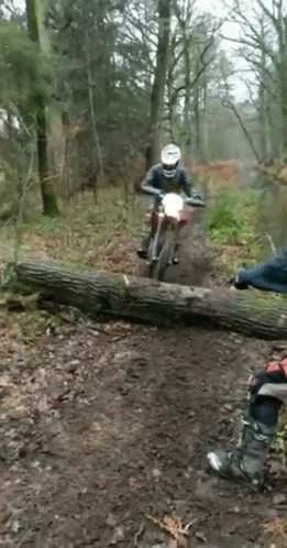 A Man On A Dirt Bike Is Riding Over A Log GIF