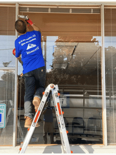 a man on a ladder wearing a blue shirt that says ' in glass install llc '